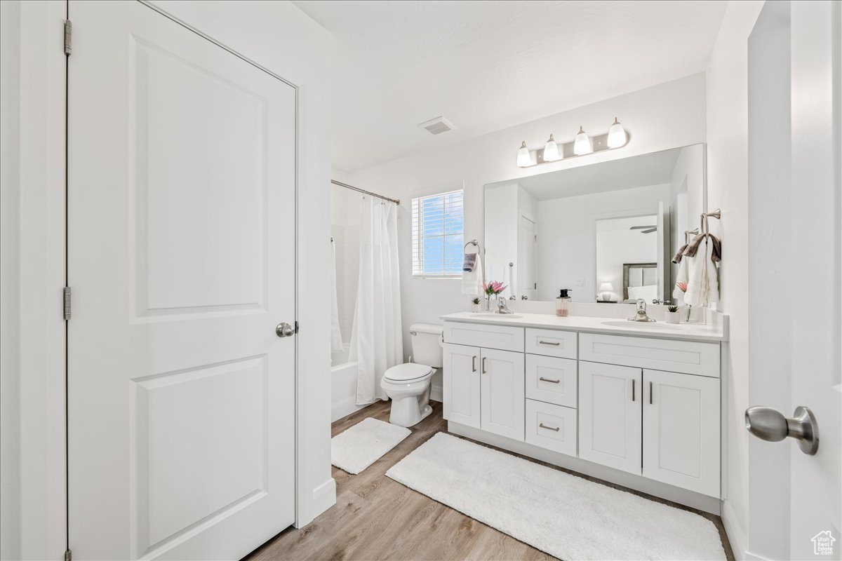 Bathroom with visible vents, toilet, a sink, wood finished floors, and double vanity