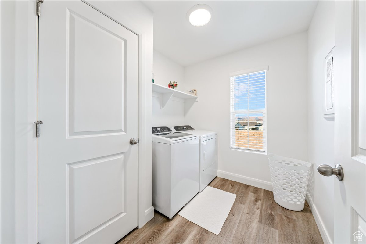 Clothes washing area with washer and clothes dryer, laundry area, baseboards, and light wood-style floors