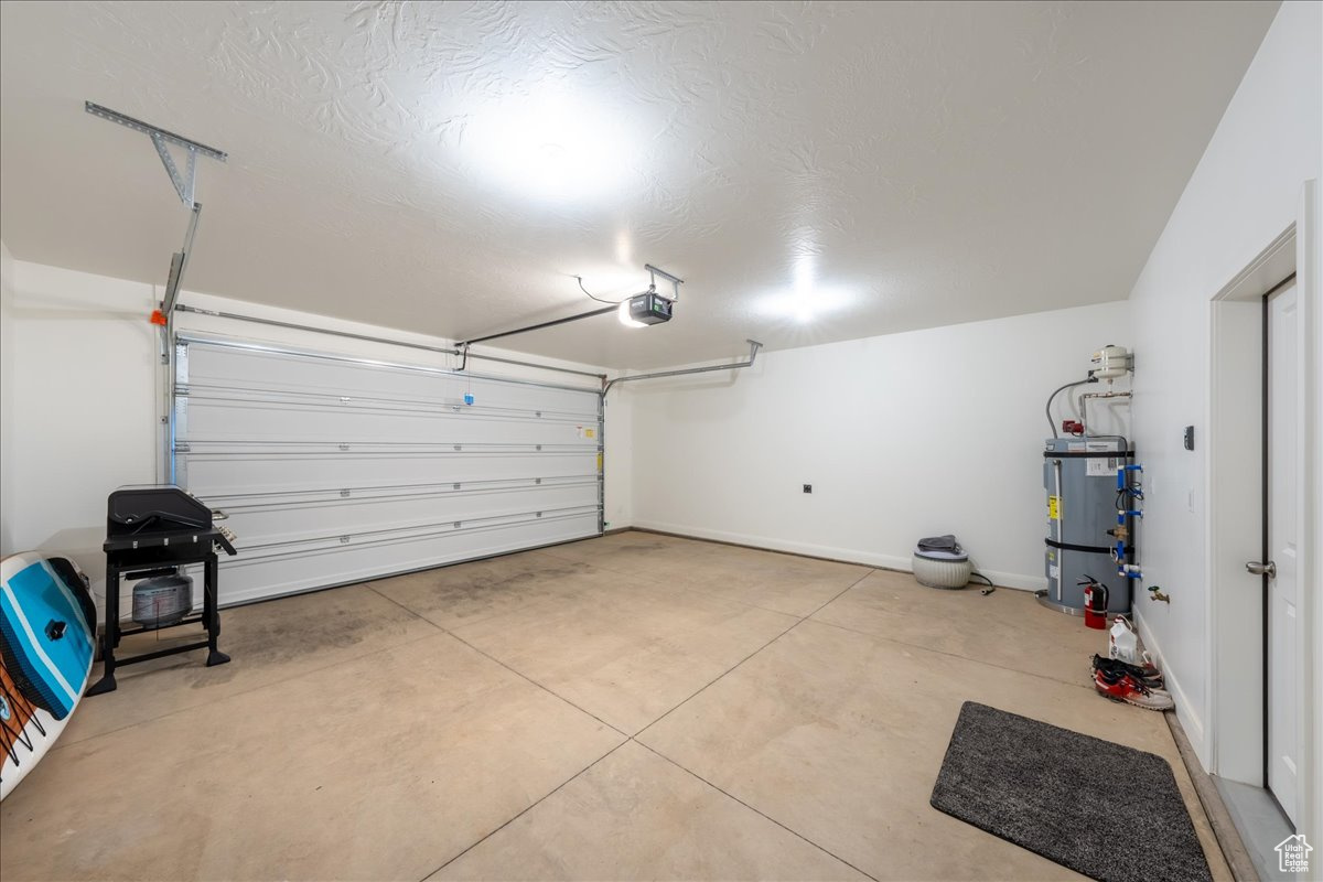 Garage with baseboards, a garage door opener, and water heater