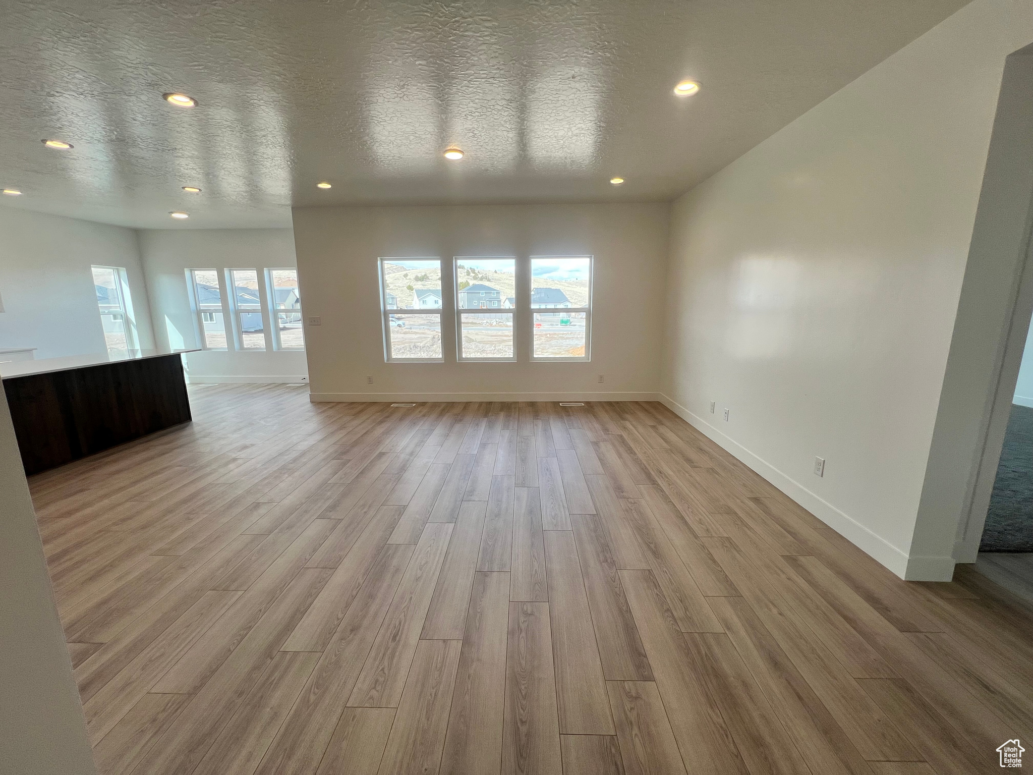 Unfurnished living room featuring recessed lighting, baseboards, light wood-style floors, and a textured ceiling