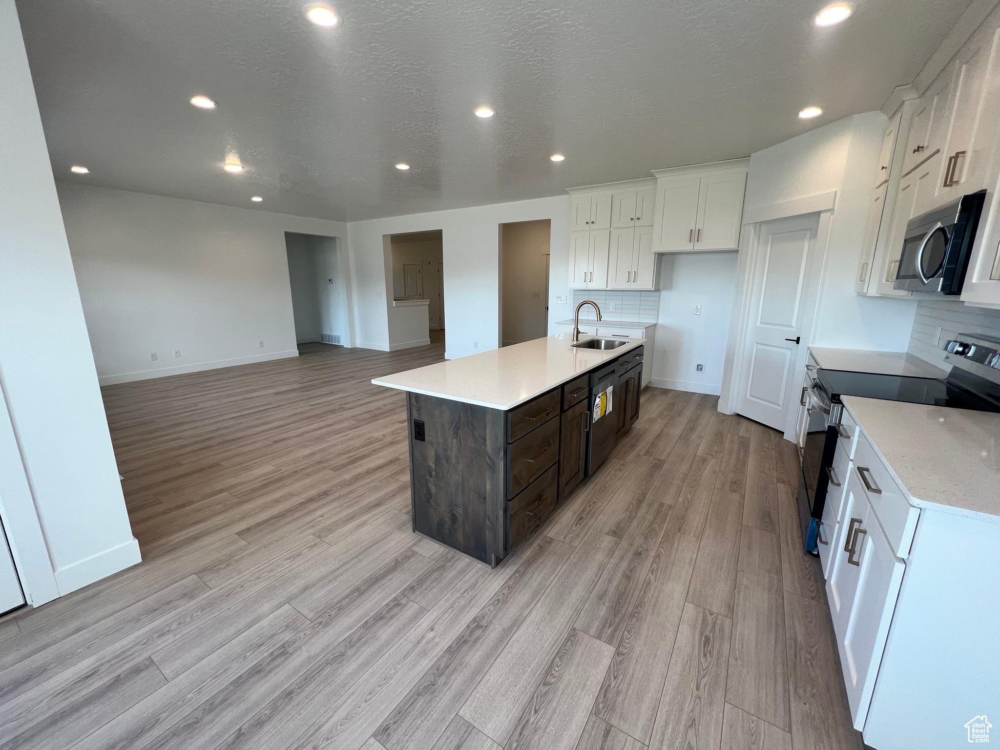 Kitchen featuring light wood-style flooring, a sink, appliances with stainless steel finishes, white cabinetry, and tasteful backsplash