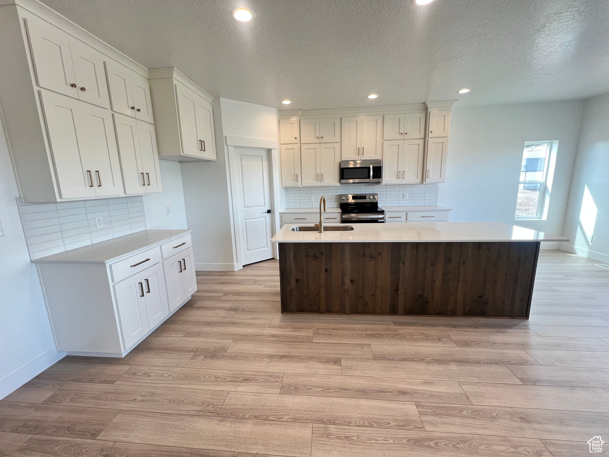 Kitchen featuring appliances with stainless steel finishes, white cabinetry, light countertops, and a sink