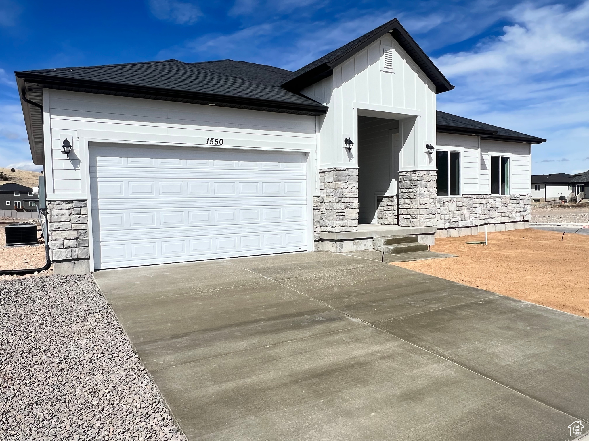 View of front facade featuring stone siding, concrete driveway, an attached garage, and a shingled roof