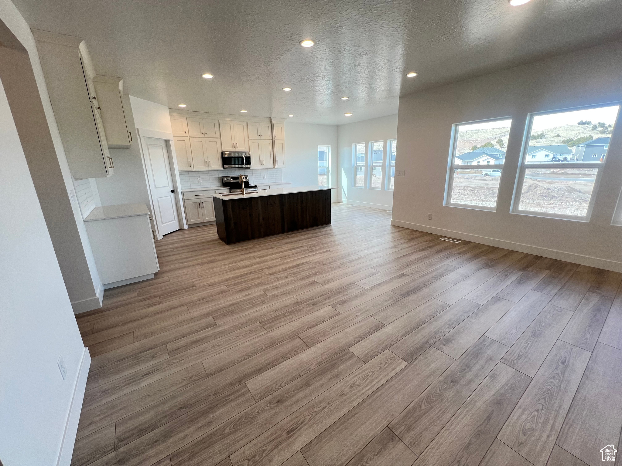Kitchen with light wood-style flooring, open floor plan, appliances with stainless steel finishes, light countertops, and decorative backsplash