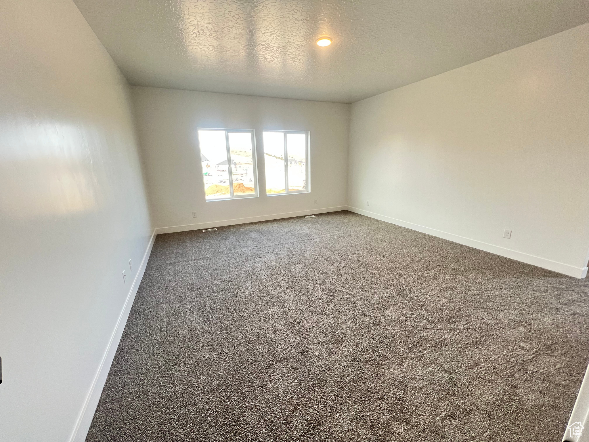 Empty room featuring a textured ceiling, baseboards, and carpet floors