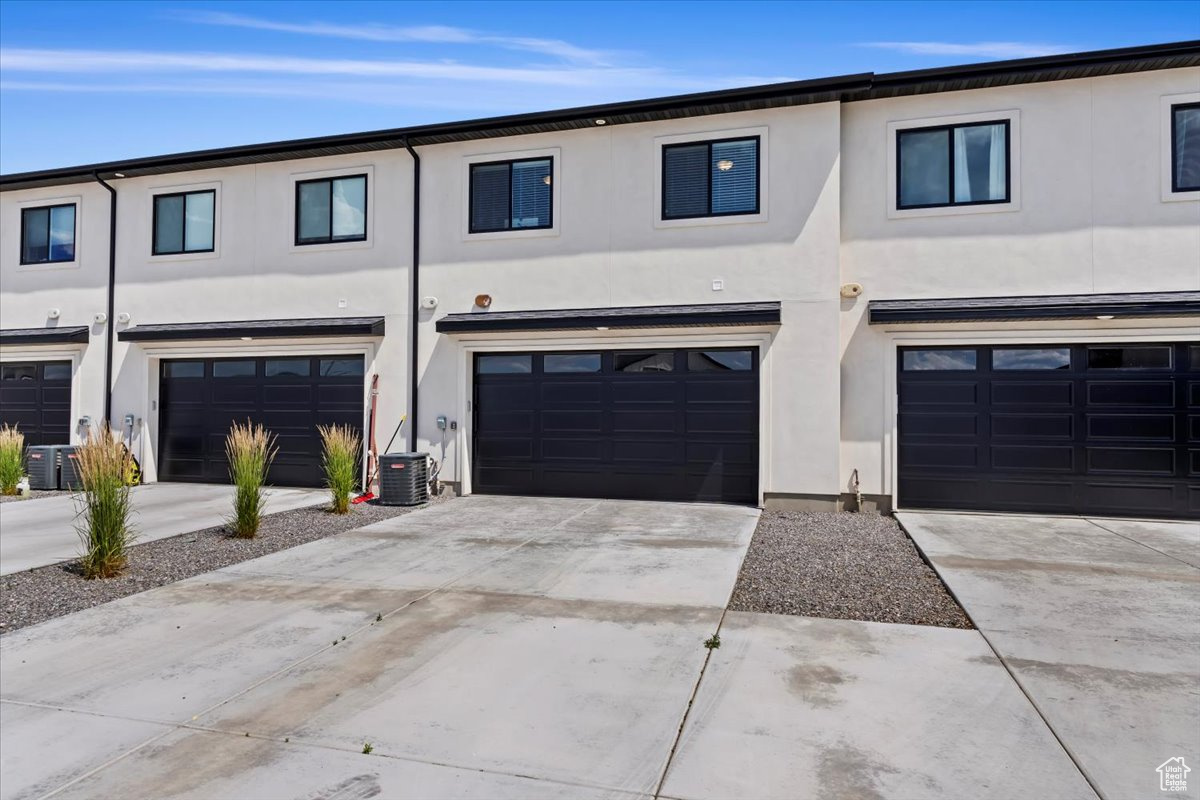 View of property with concrete driveway, an attached garage, cooling unit, and stucco siding