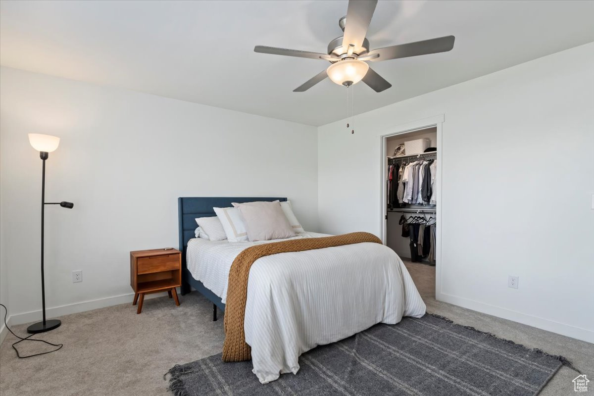 Carpeted bedroom with a closet, ceiling fan, a walk in closet, and baseboards