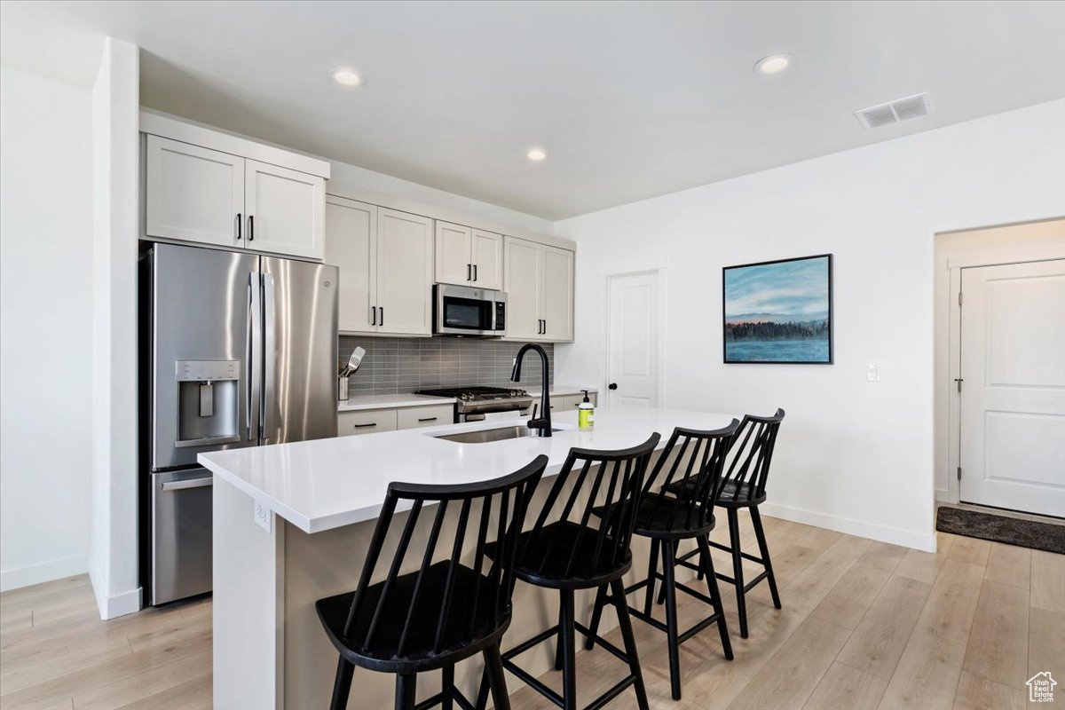 Kitchen with tasteful backsplash, light wood finished floors, a sink, appliances with stainless steel finishes, and a kitchen island with sink