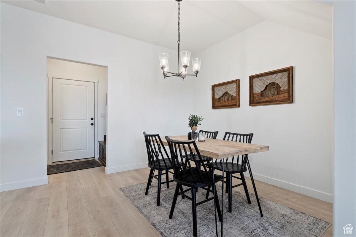 Dining space featuring an inviting chandelier, baseboards, light wood-type flooring, and lofted ceiling