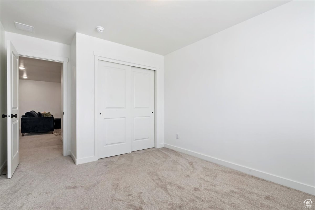 Unfurnished bedroom with a closet, baseboards, and light colored carpet