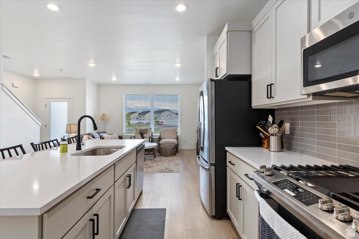 Kitchen featuring a sink, decorative backsplash, light countertops, appliances with stainless steel finishes, and light wood-type flooring