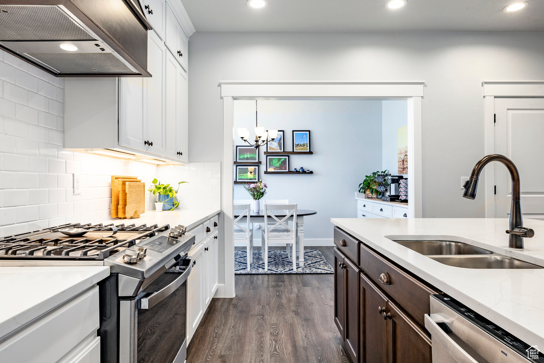 Kitchen featuring dark brown cabinets, dark wood-type flooring, wall chimney range hood, appliances with stainless steel finishes, and a sink