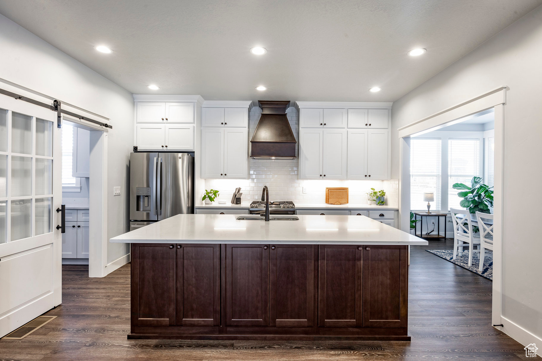 Kitchen featuring light countertops, a barn door, custom exhaust hood, stainless steel fridge, and a sink