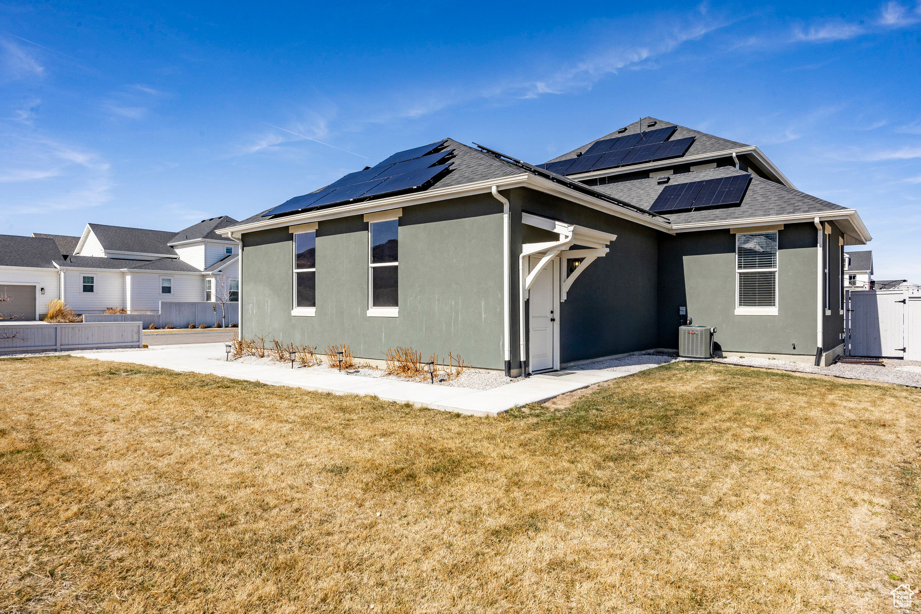 Rear view of property with stucco siding, a lawn, solar panels, and a shingled roof