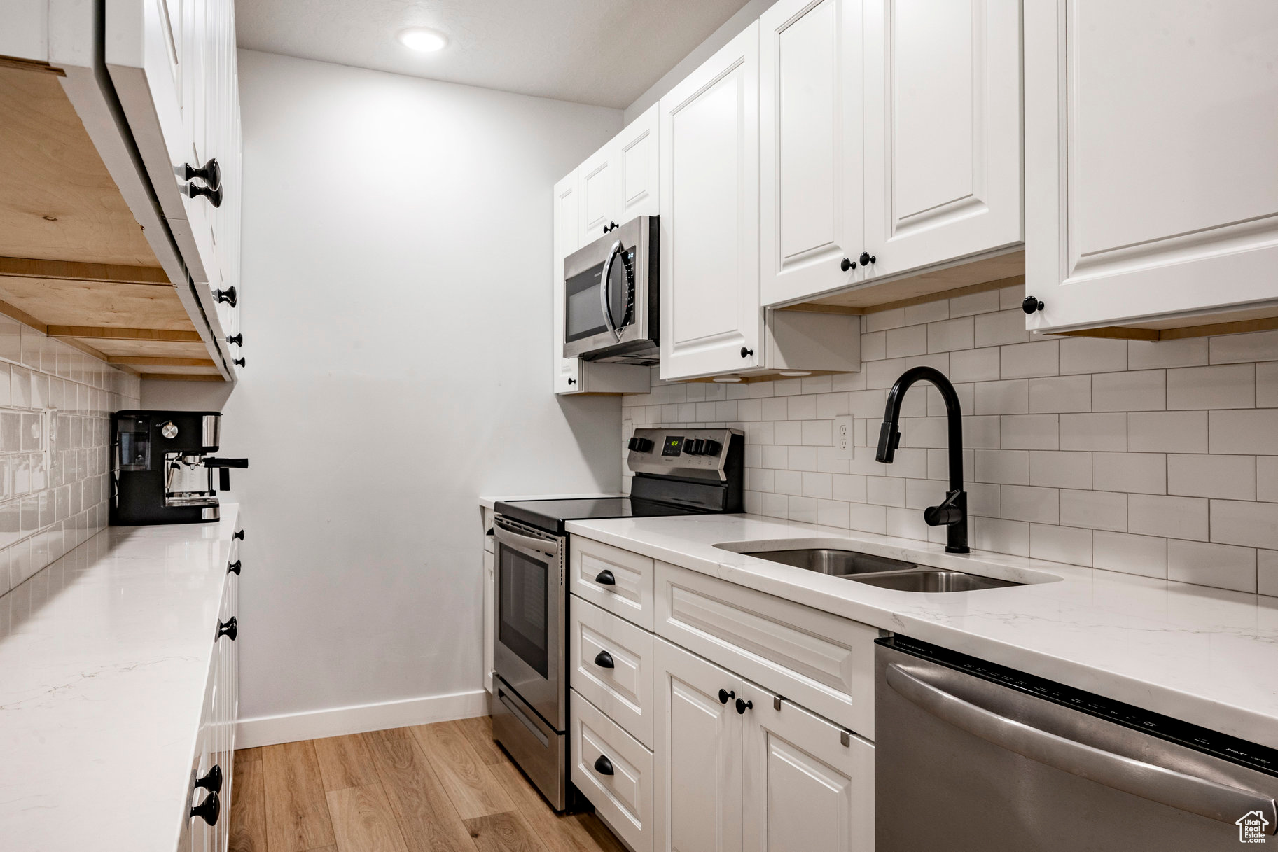 Kitchen featuring light wood finished floors, baseboards, appliances with stainless steel finishes, white cabinetry, and a sink