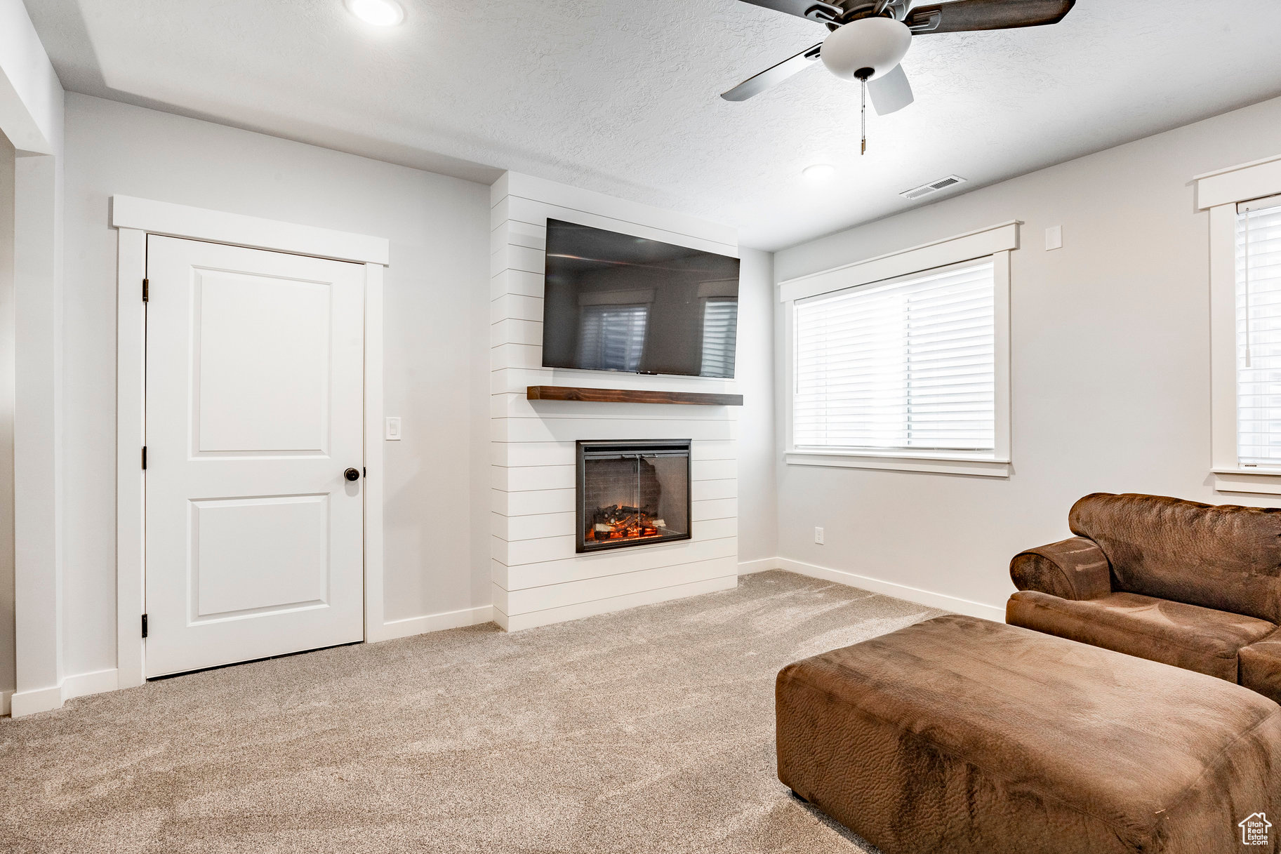 Carpeted living room featuring visible vents, baseboards, a fireplace, ceiling fan, and a textured ceiling
