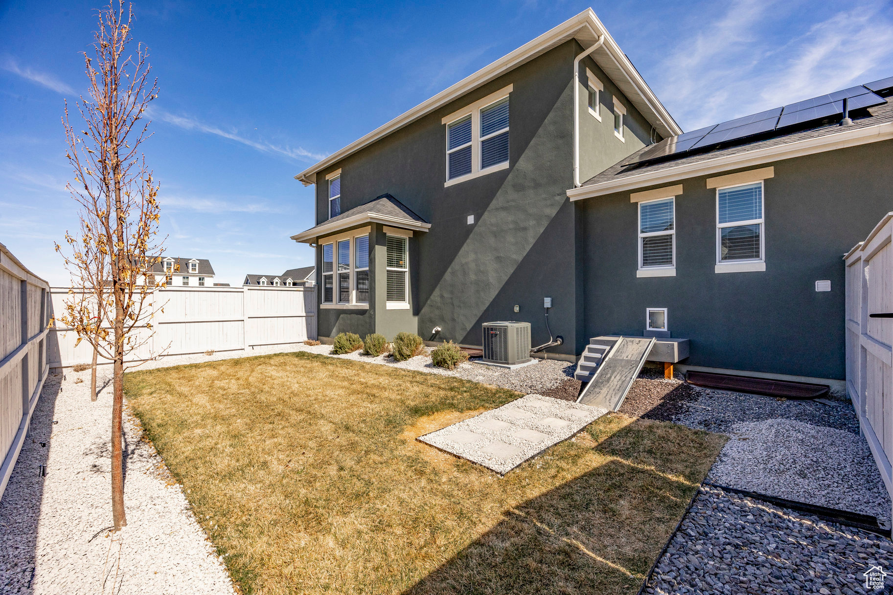 Rear view of property with stucco siding, roof mounted solar panels, a fenced backyard, cooling unit, and a yard