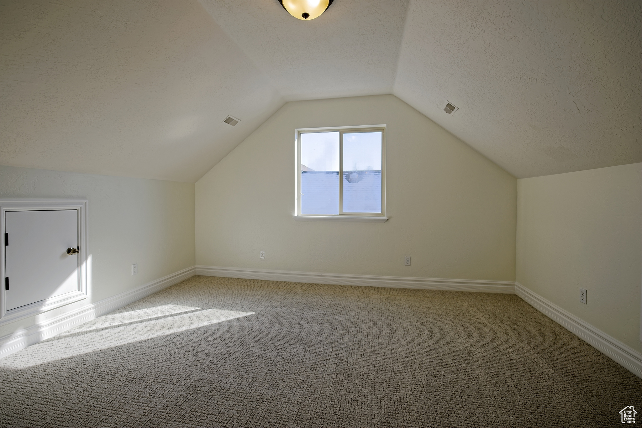 Additional living space with a textured ceiling, lofted ceiling, and light brand new carpet