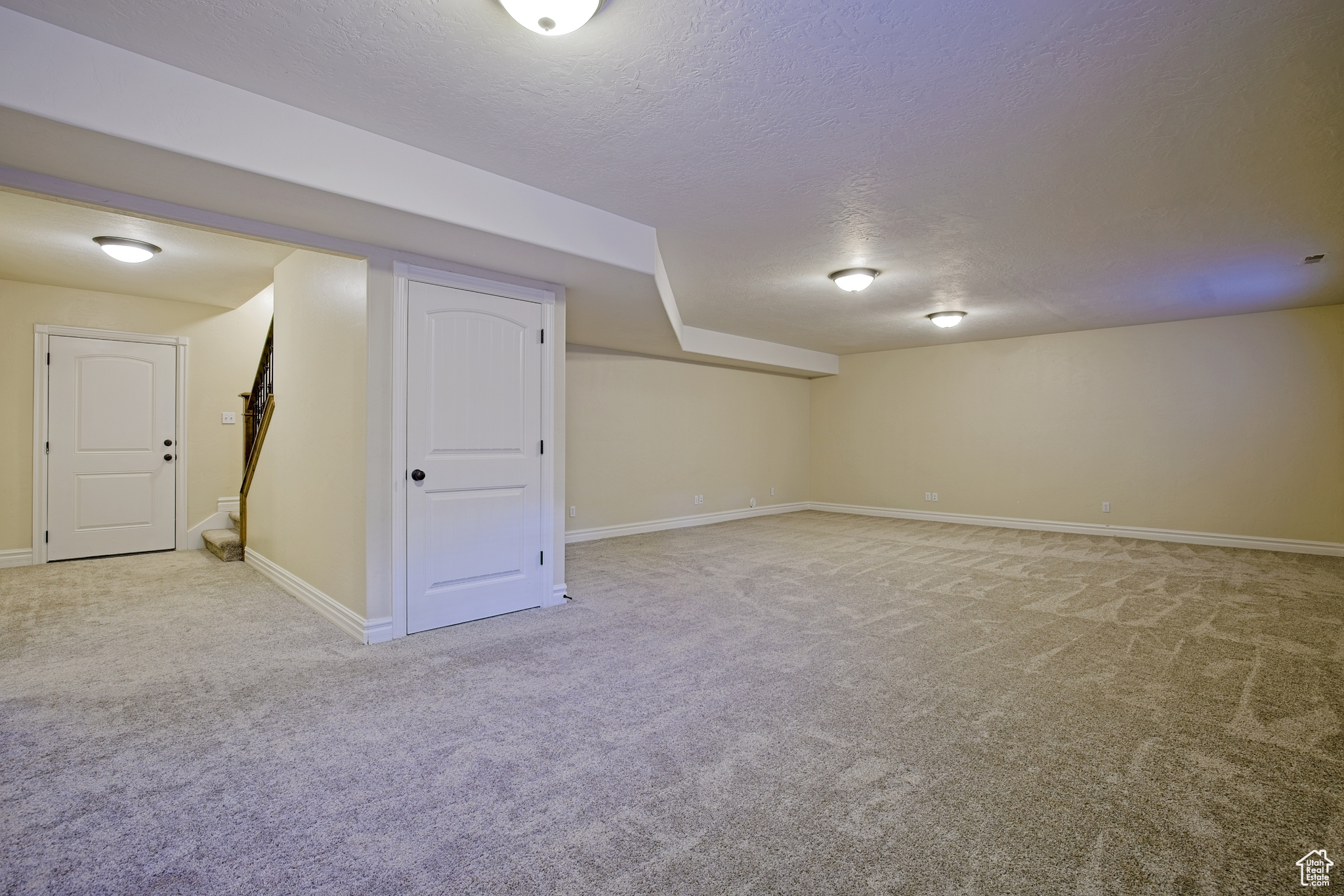 Finished basement featuring a textured ceiling, stairway, baseboards, and light carpet
