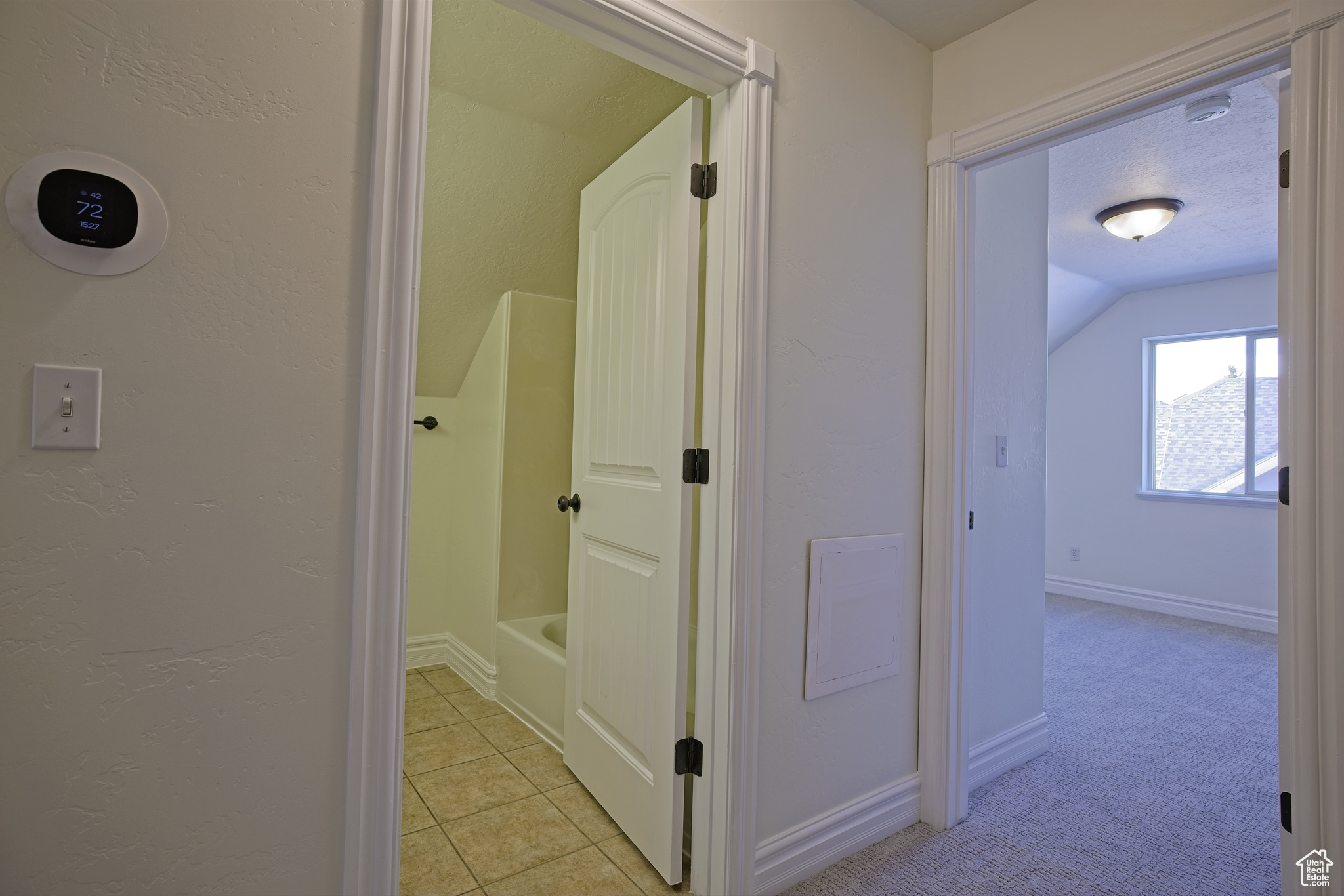 Hall with baseboards, lofted ceiling, light carpet, light tile patterned flooring, and a textured ceiling