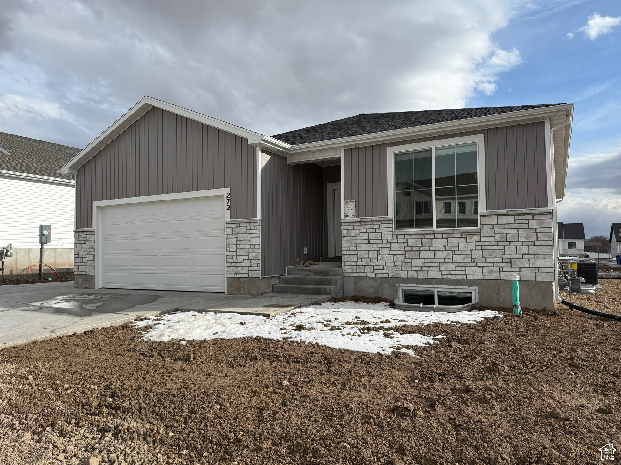 Ranch-style house featuring a shingled roof, concrete driveway, central AC unit, a garage, and stone siding