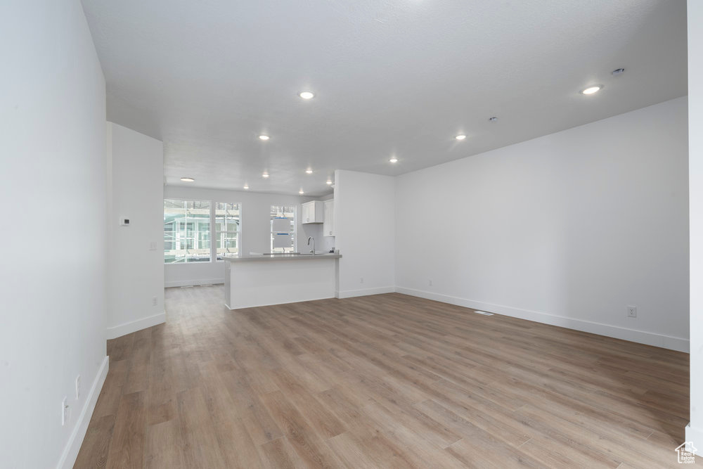 Unfurnished living room with recessed lighting, light wood-type flooring, baseboards, and a sink