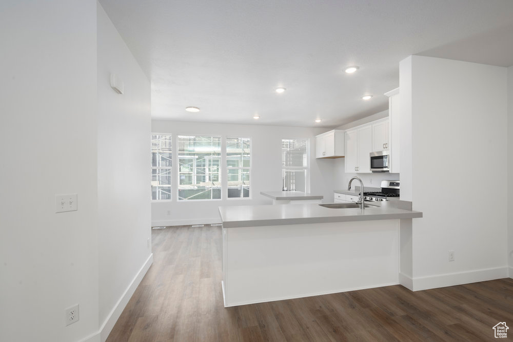 Kitchen with a sink, wood finished floors, appliances with stainless steel finishes, white cabinets, and light countertops