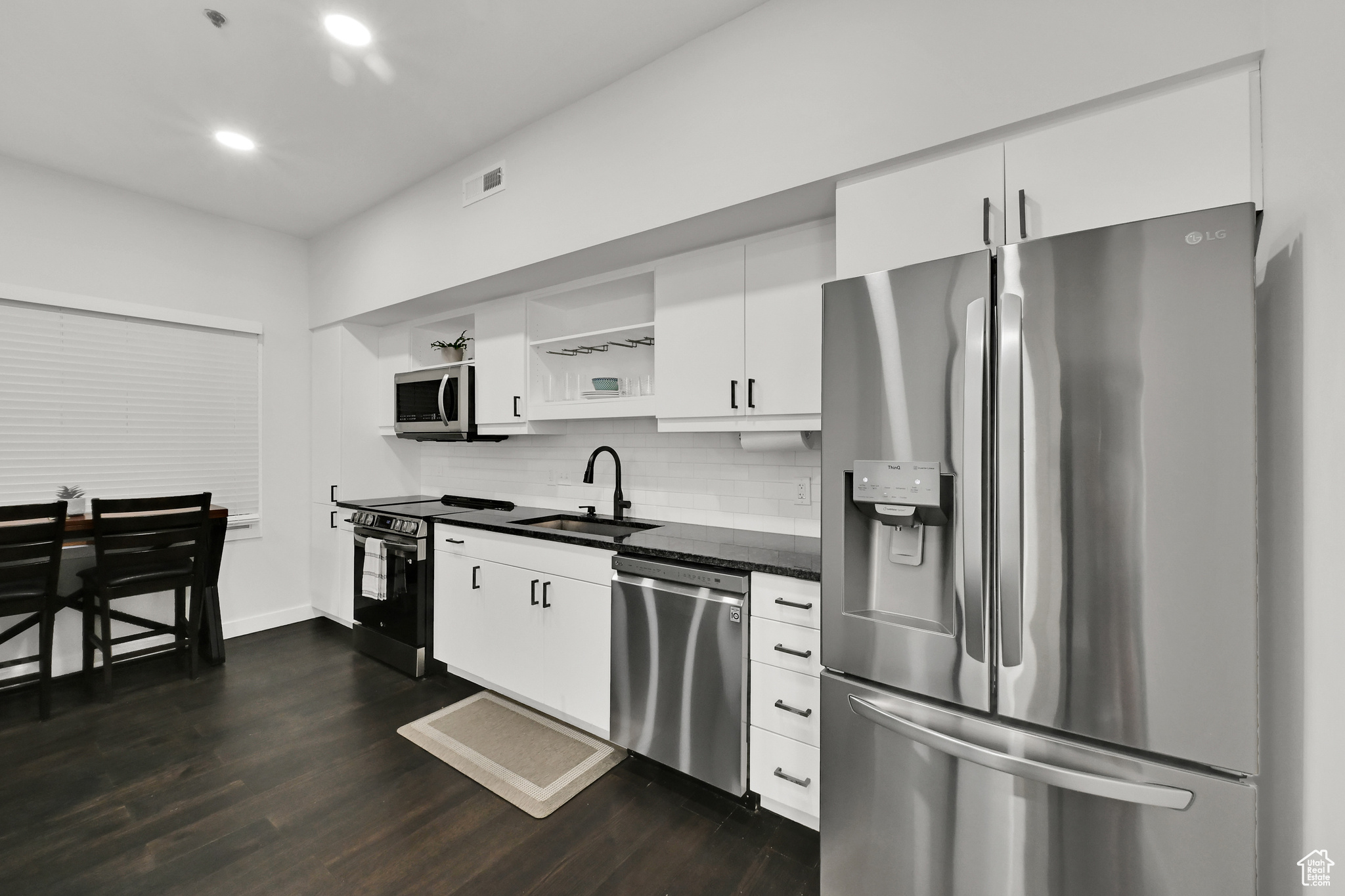Kitchen featuring dark countertops, visible vents, decorative backsplash, stainless steel appliances, and a sink