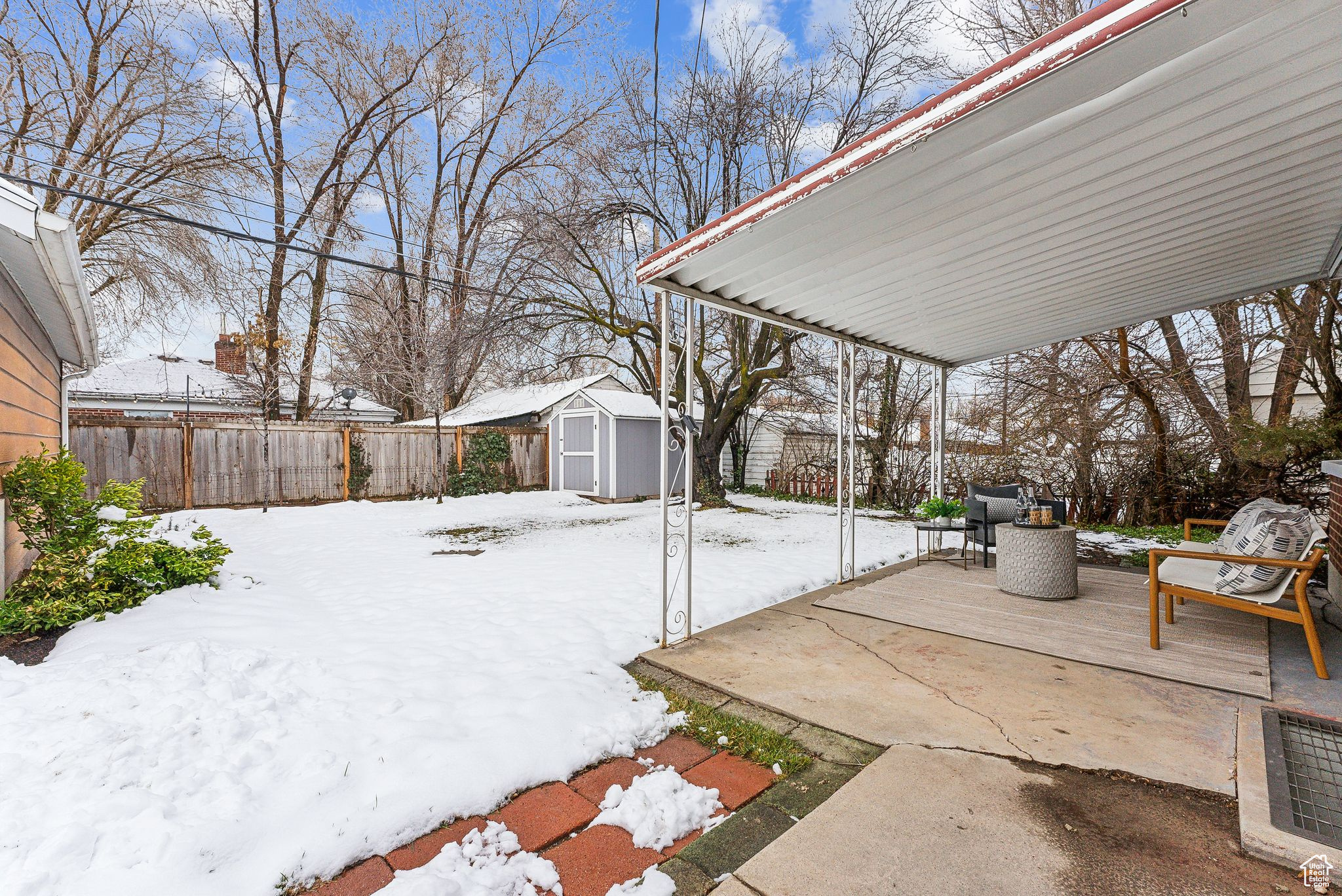 Yard layered in snow featuring a fenced backyard, a patio, a storage shed, and an outdoor structure