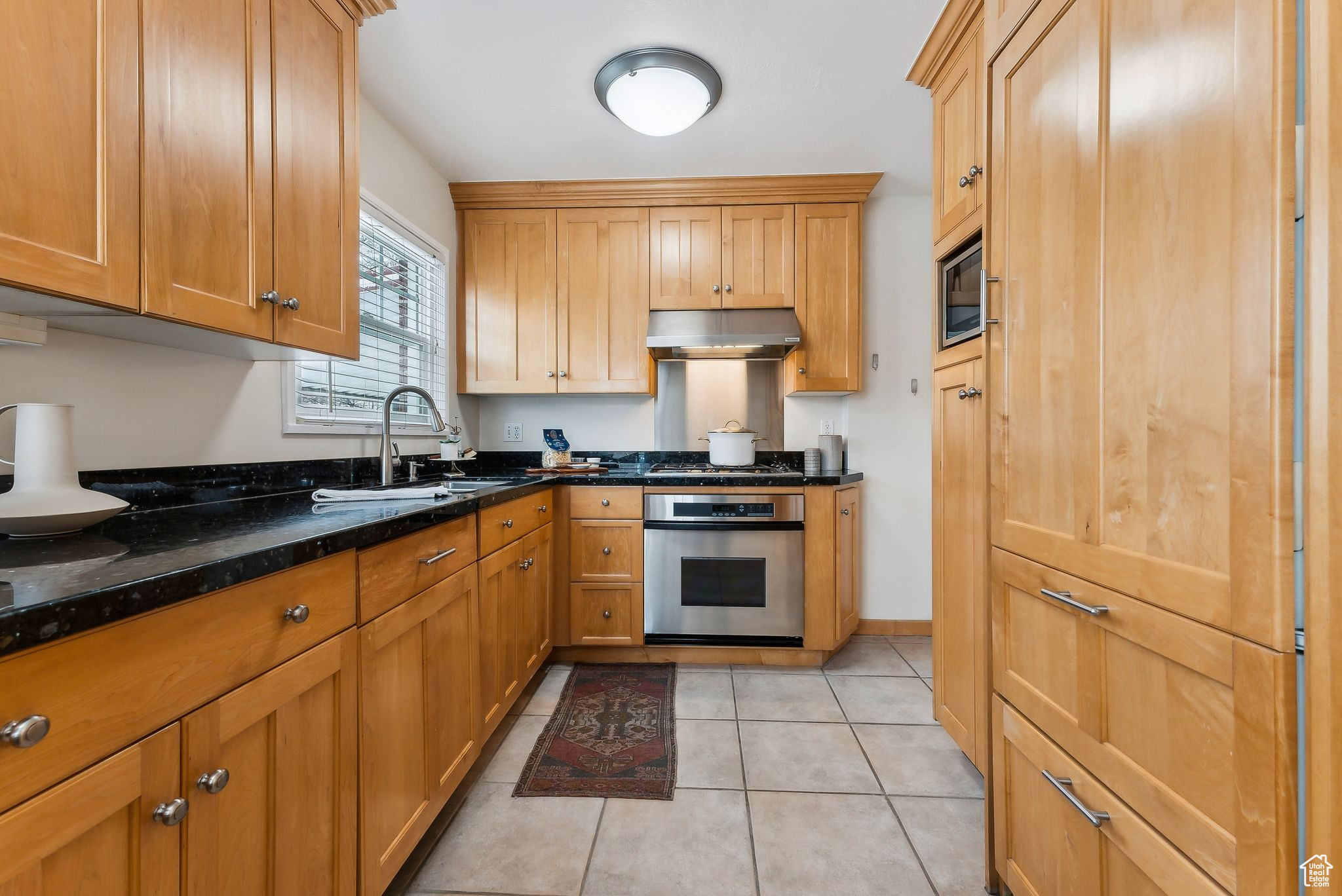 Kitchen with light tile patterned flooring, built in microwave, a sink, under cabinet range hood, and stainless steel oven