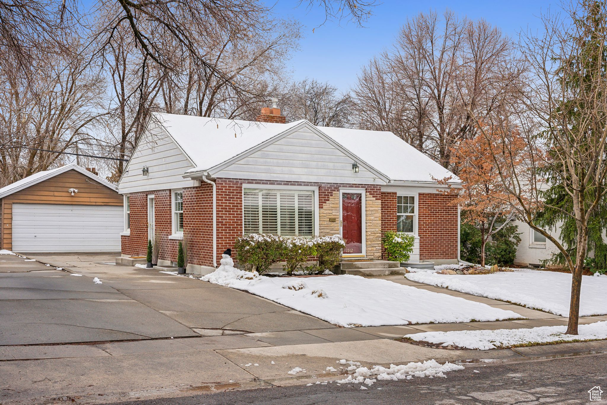 View of front of home with brick siding, a chimney, a garage, and an outdoor structure