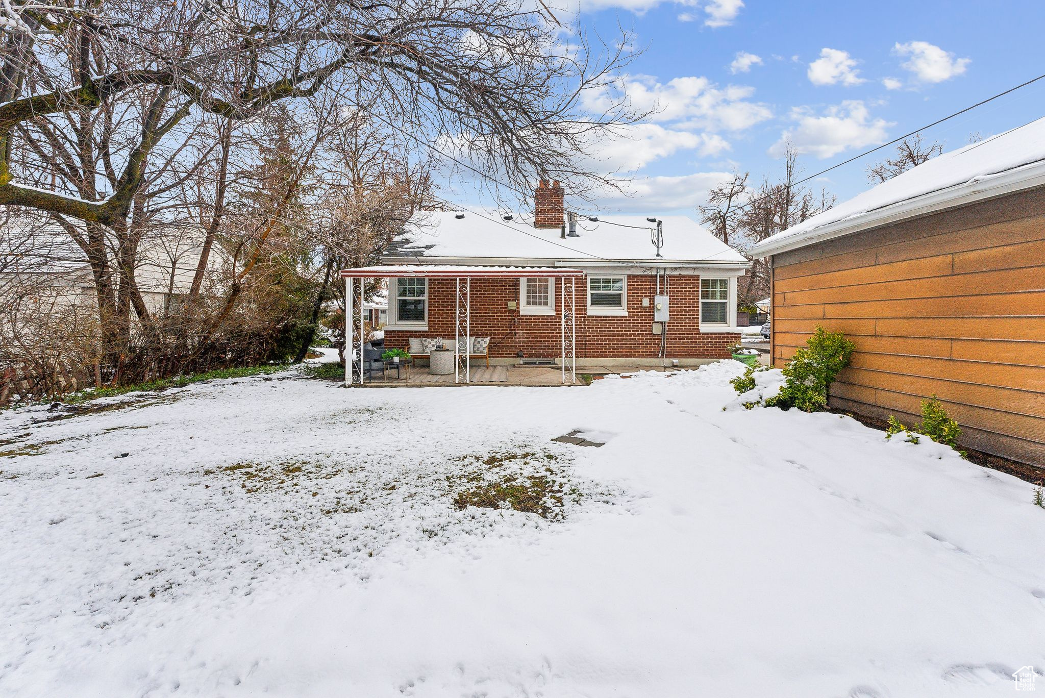 Snow covered back of property featuring brick siding and a chimney