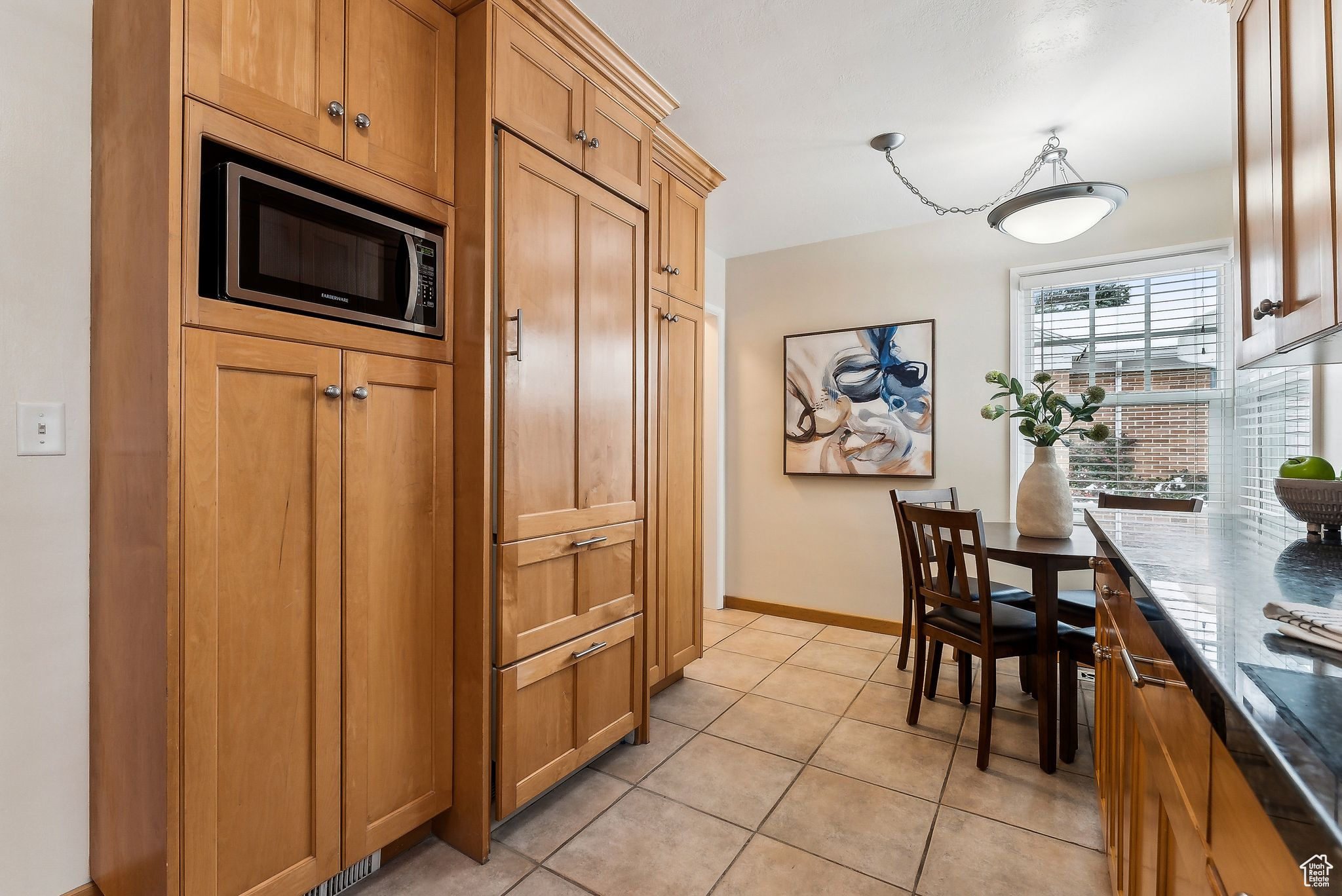 Kitchen with light tile patterned floors, baseboards, dark stone counters, stainless steel microwave, and brown cabinets