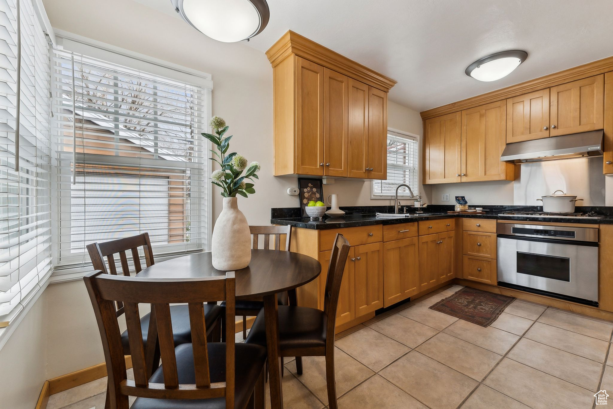 Kitchen featuring dark countertops, under cabinet range hood, light tile patterned floors, appliances with stainless steel finishes, and a sink