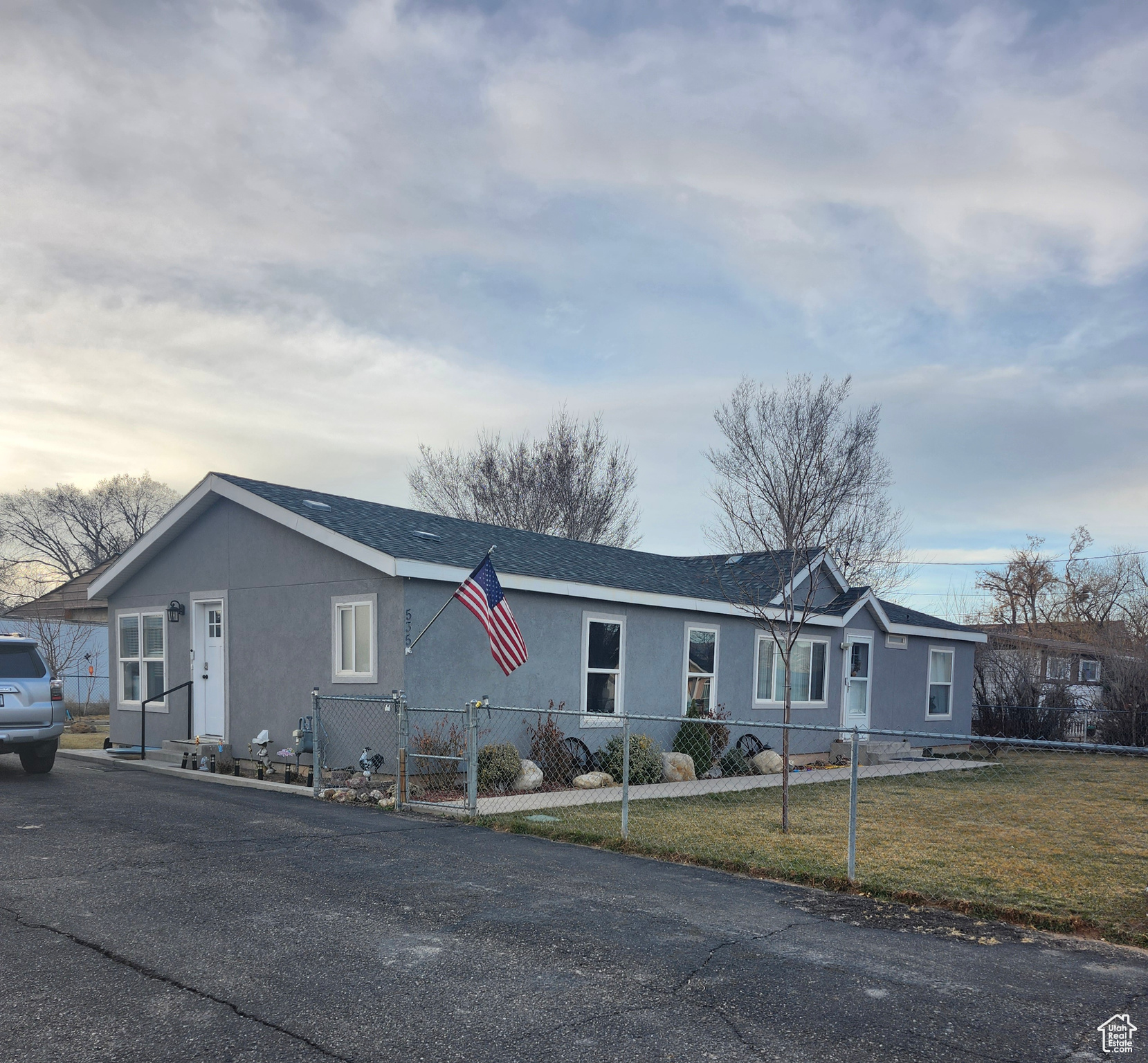 Ranch-style house with a shingled roof, a front lawn, a fenced front yard, and stucco siding