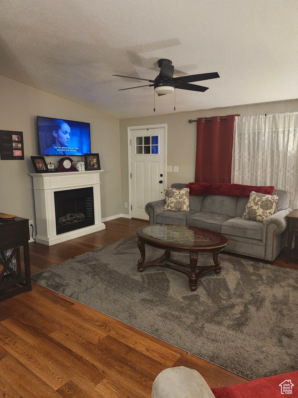 Living area with a ceiling fan, a textured ceiling, wood finished floors, and a fireplace