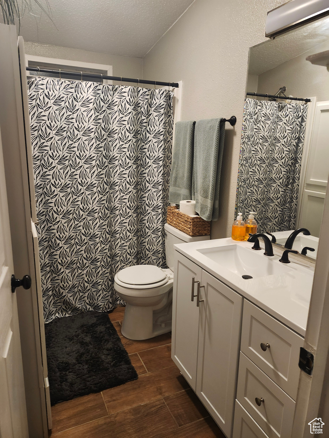 Full bathroom featuring wood finish floors, toilet, curtained shower, a textured ceiling, and vanity