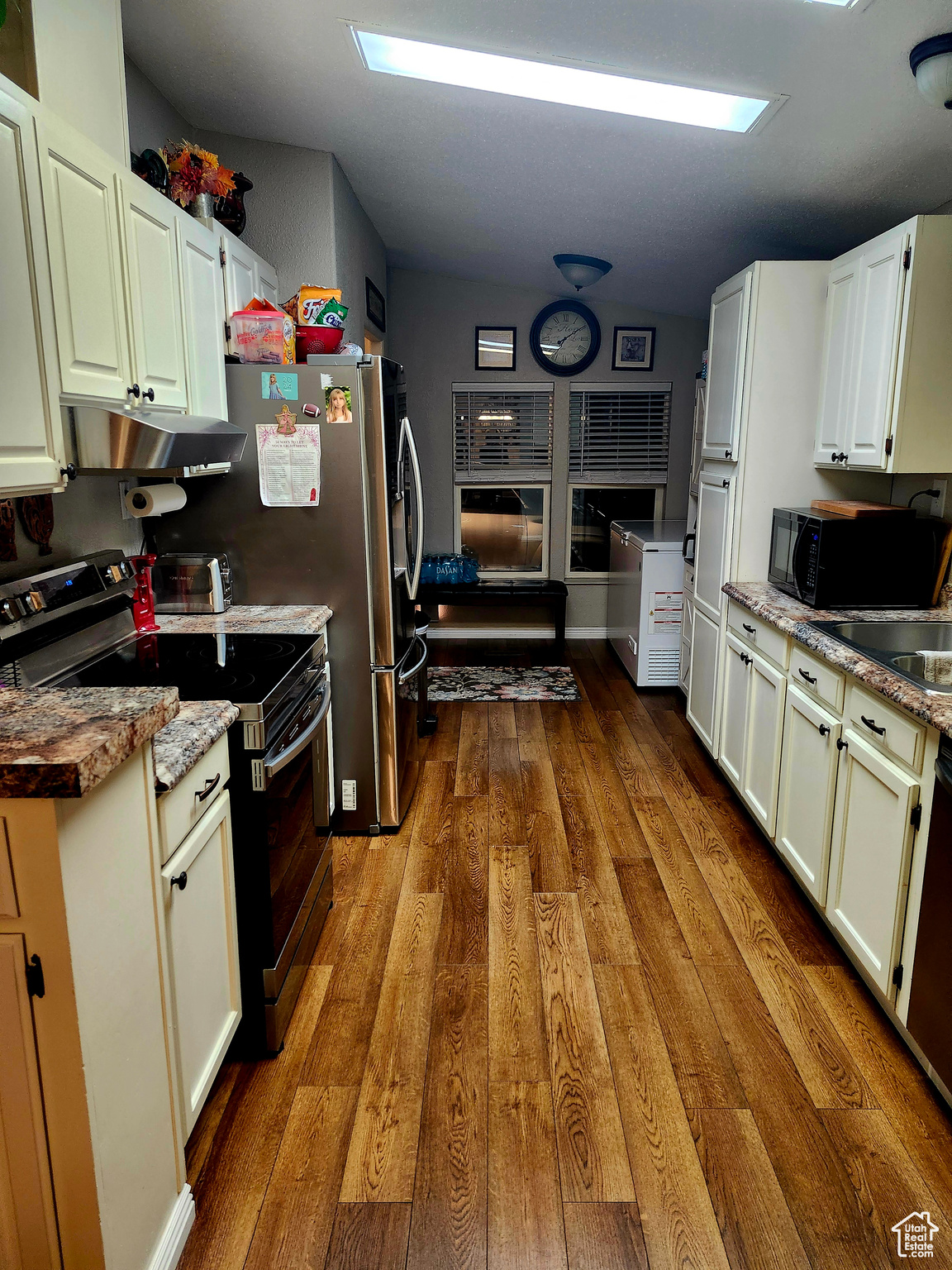 Kitchen featuring wood finished floors, stainless steel range with electric cooktop, black microwave, under cabinet range hood, and white cabinetry