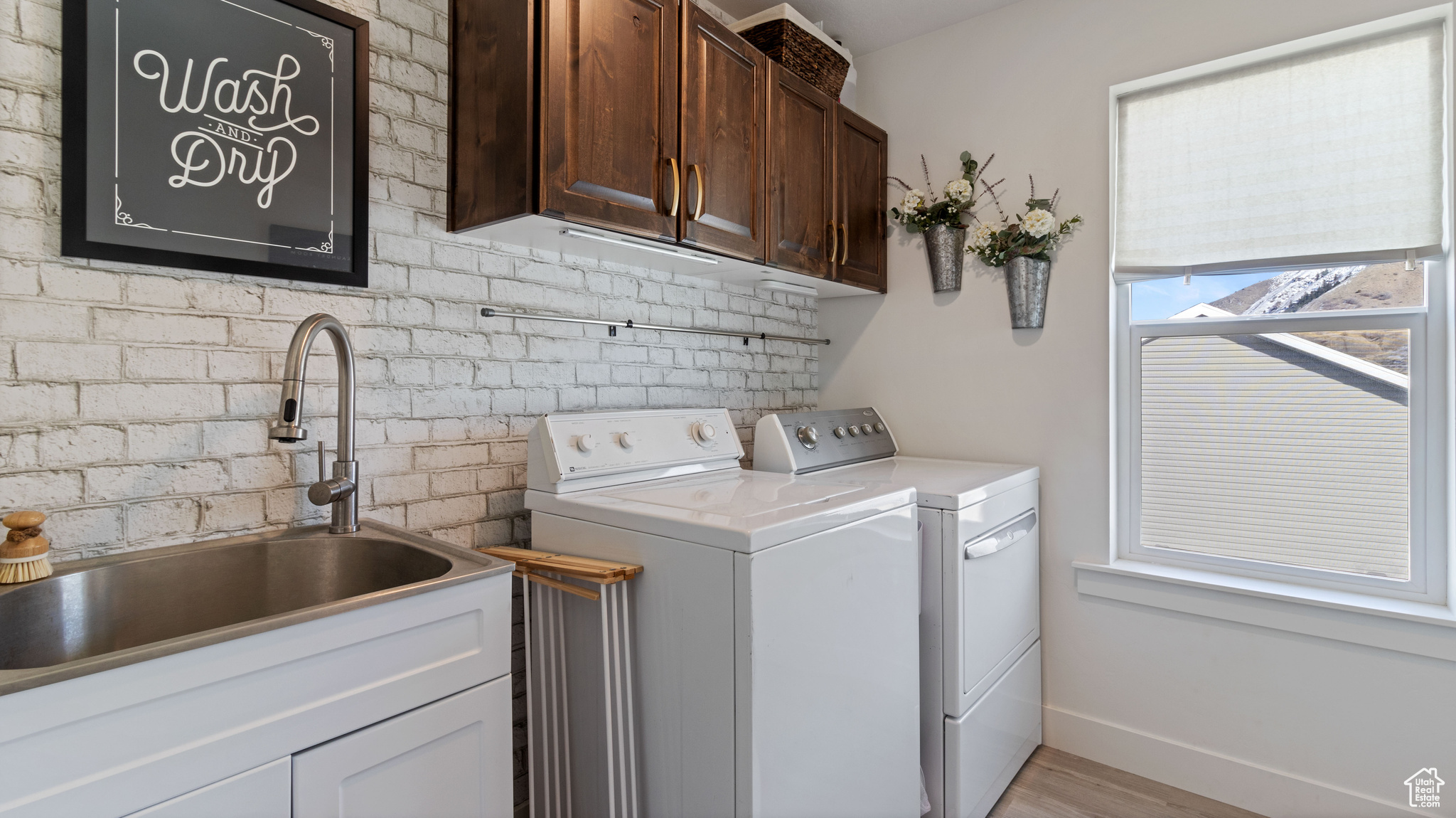 Clothes washing area featuring a sink, cabinet space, brick wall, baseboards, and washing machine and clothes dryer