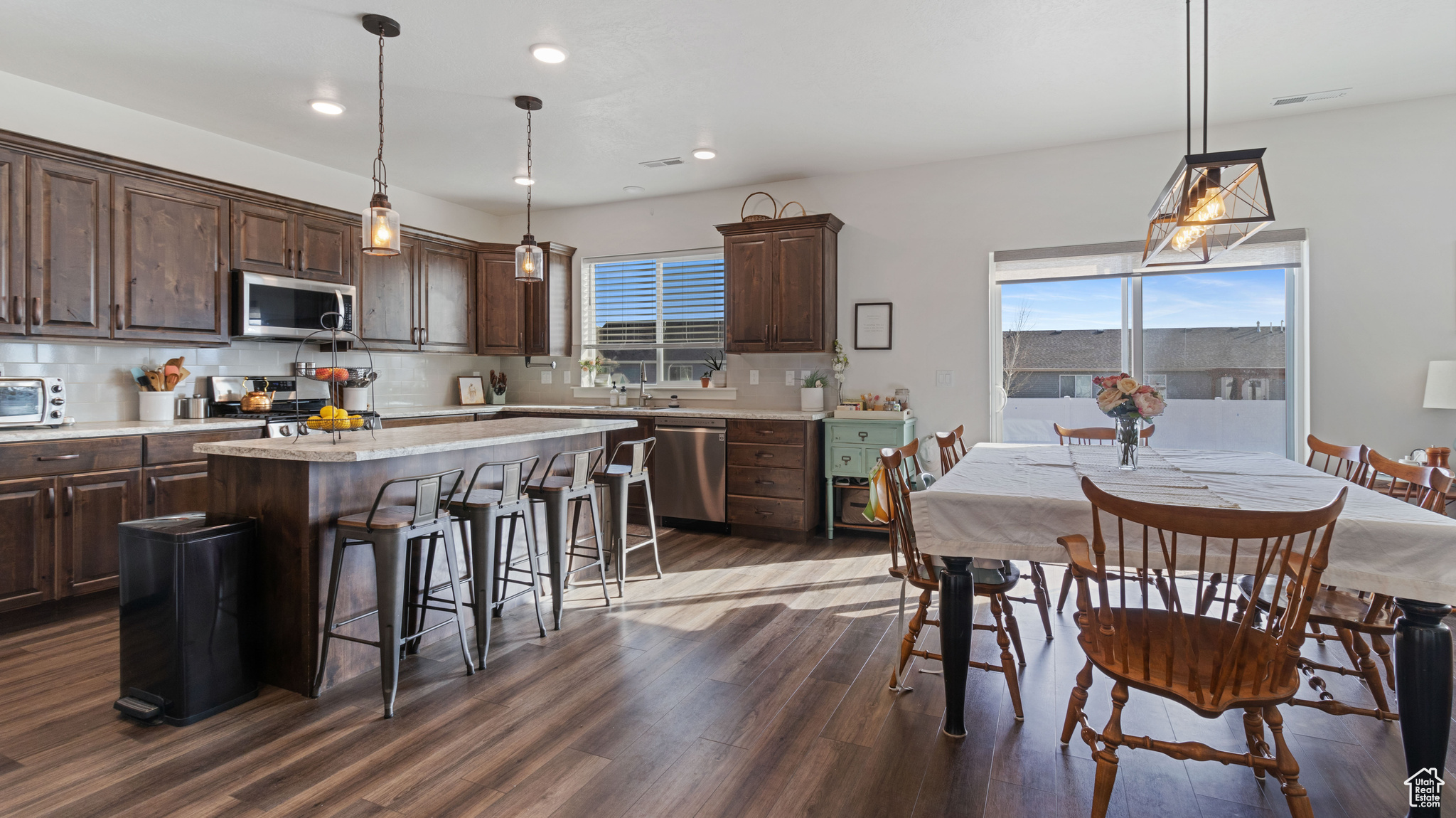 Kitchen with dark brown cabinetry, backsplash, appliances with stainless steel finishes, and a breakfast bar area