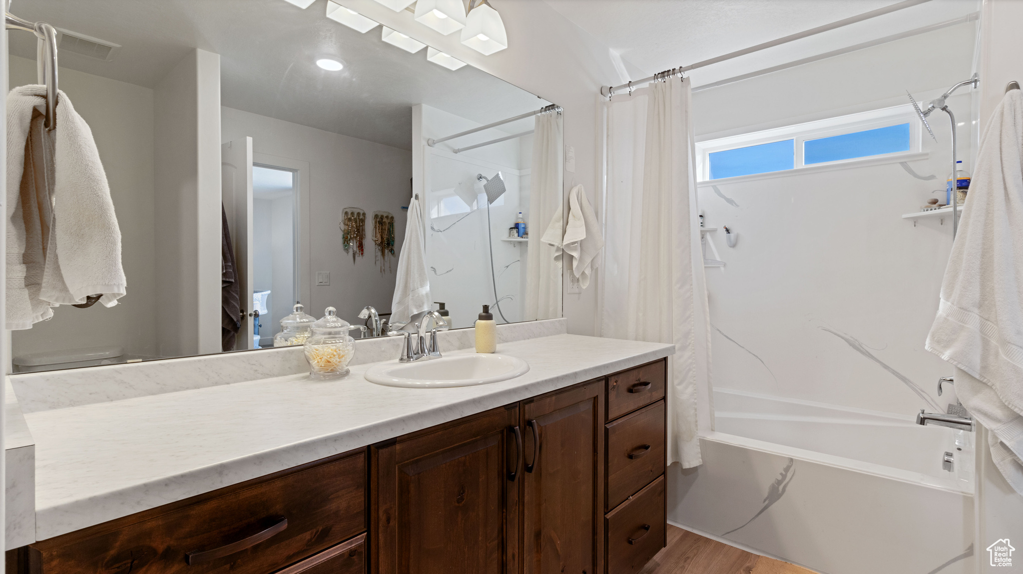 Bathroom with vanity, wood finished floors, and shower / bathtub combination with curtain