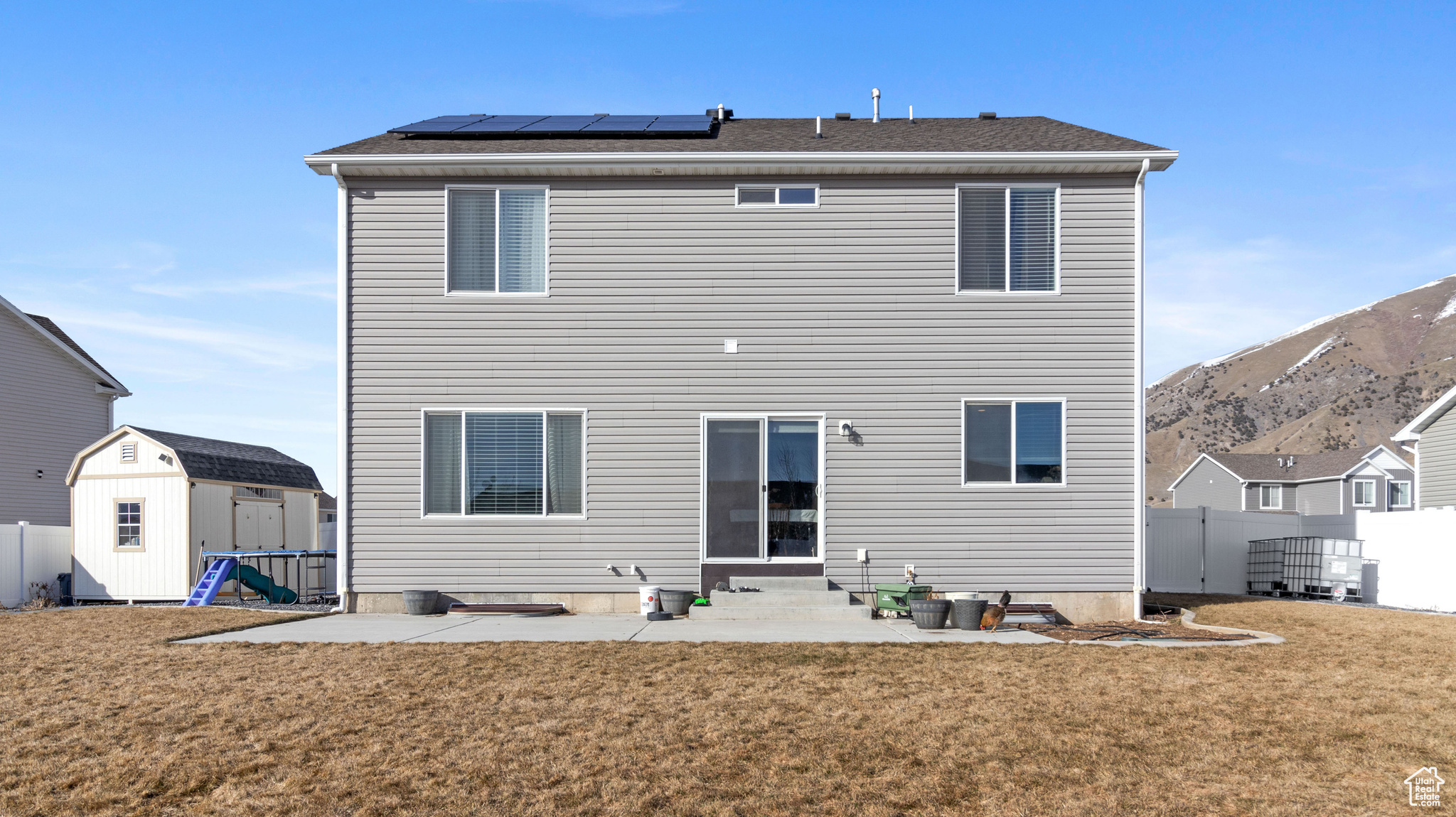 Back of house featuring a storage unit, a lawn, entry steps, an outdoor structure, and solar panels