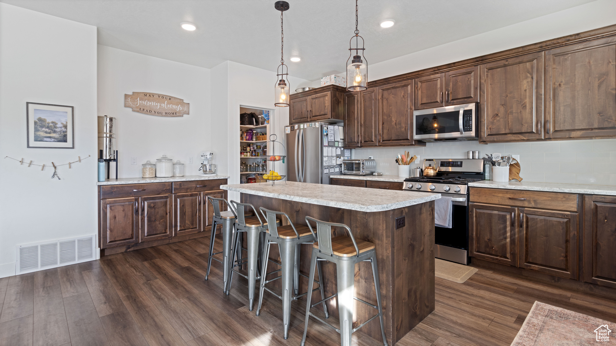 Kitchen with visible vents, a kitchen island, light countertops, appliances with stainless steel finishes, and dark wood-style LVP floors