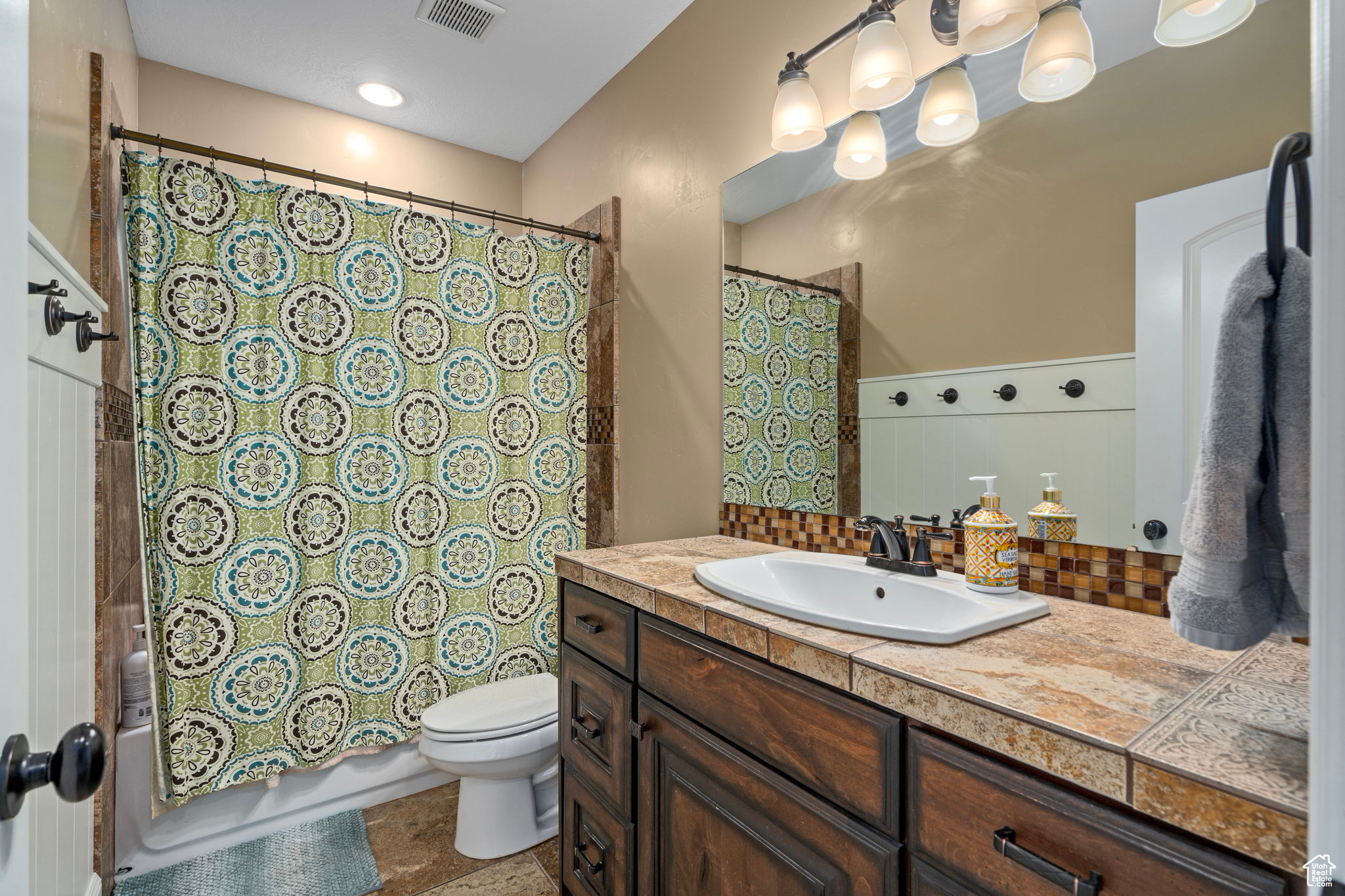 Bathroom featuring vanity, visible vents, decorative backsplash, toilet, and shower / tub combo with curtain