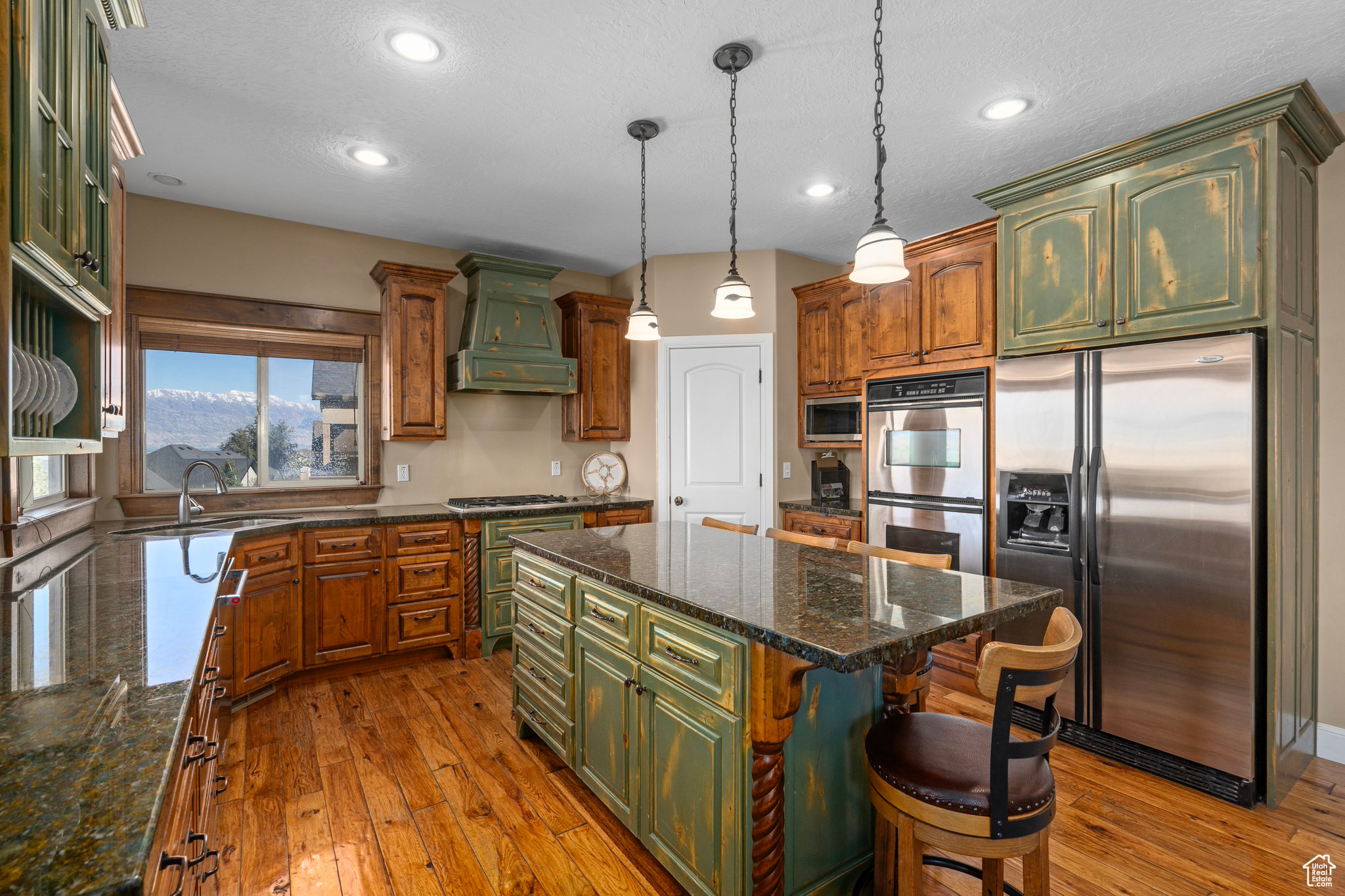 Kitchen with a kitchen island, green cabinets, custom range hood, hardwood / wood-style floors, and stainless steel appliances