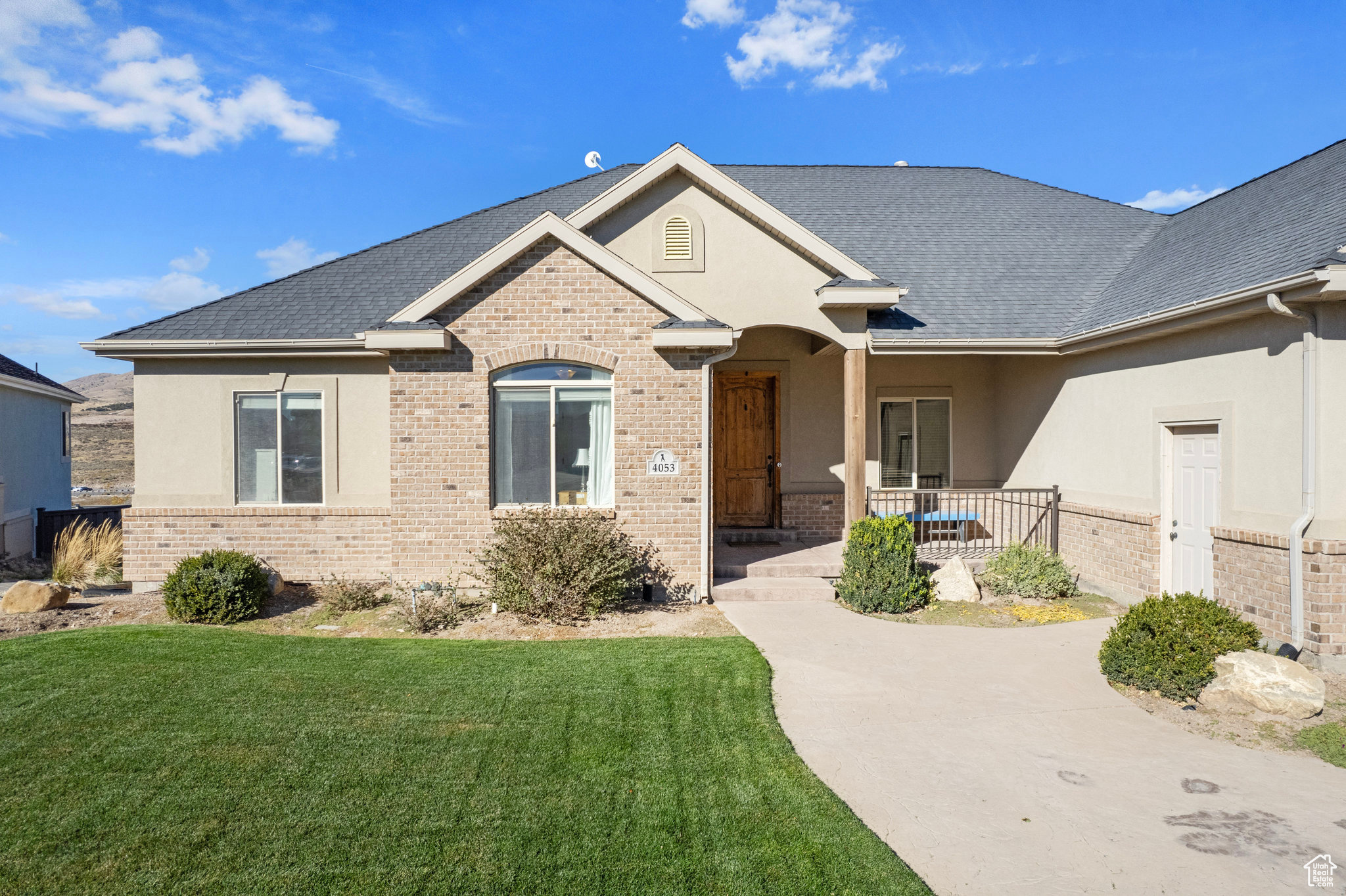 Ranch-style home with brick siding, covered porch, a shingled roof, and a front lawn
