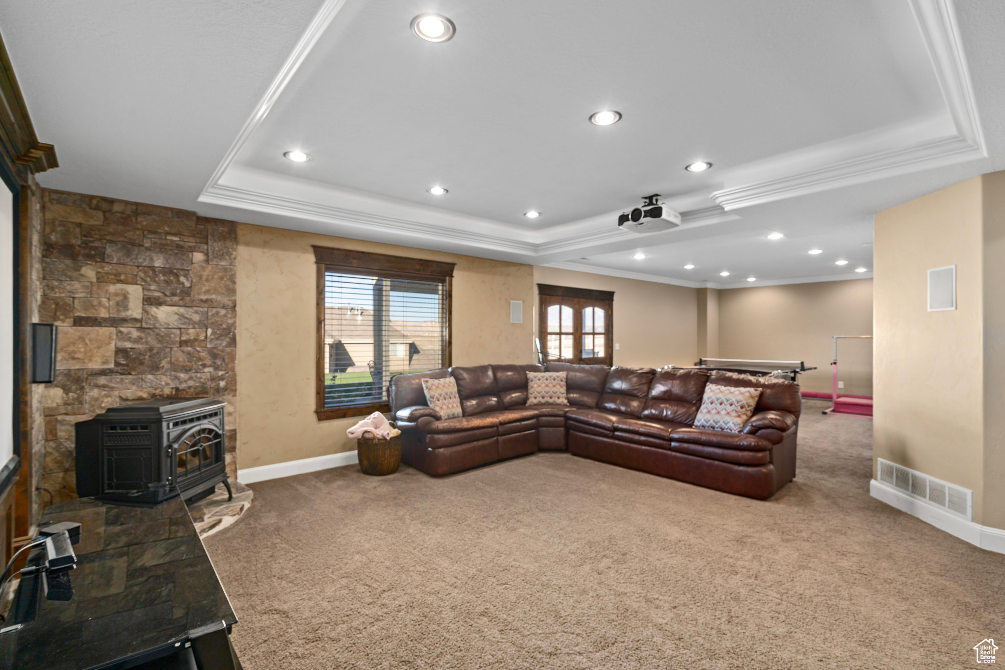 Carpeted living room with visible vents, crown molding, a raised ceiling, and baseboards