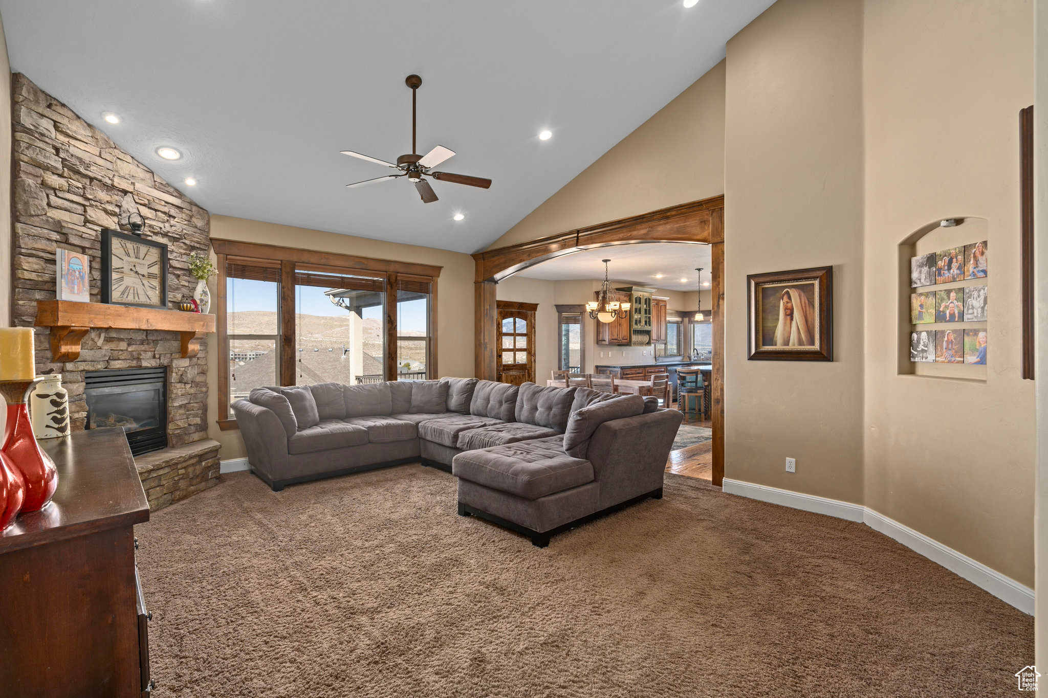 Carpeted living room featuring baseboards, high vaulted ceiling, a fireplace, arched walkways, and ceiling fan with notable chandelier