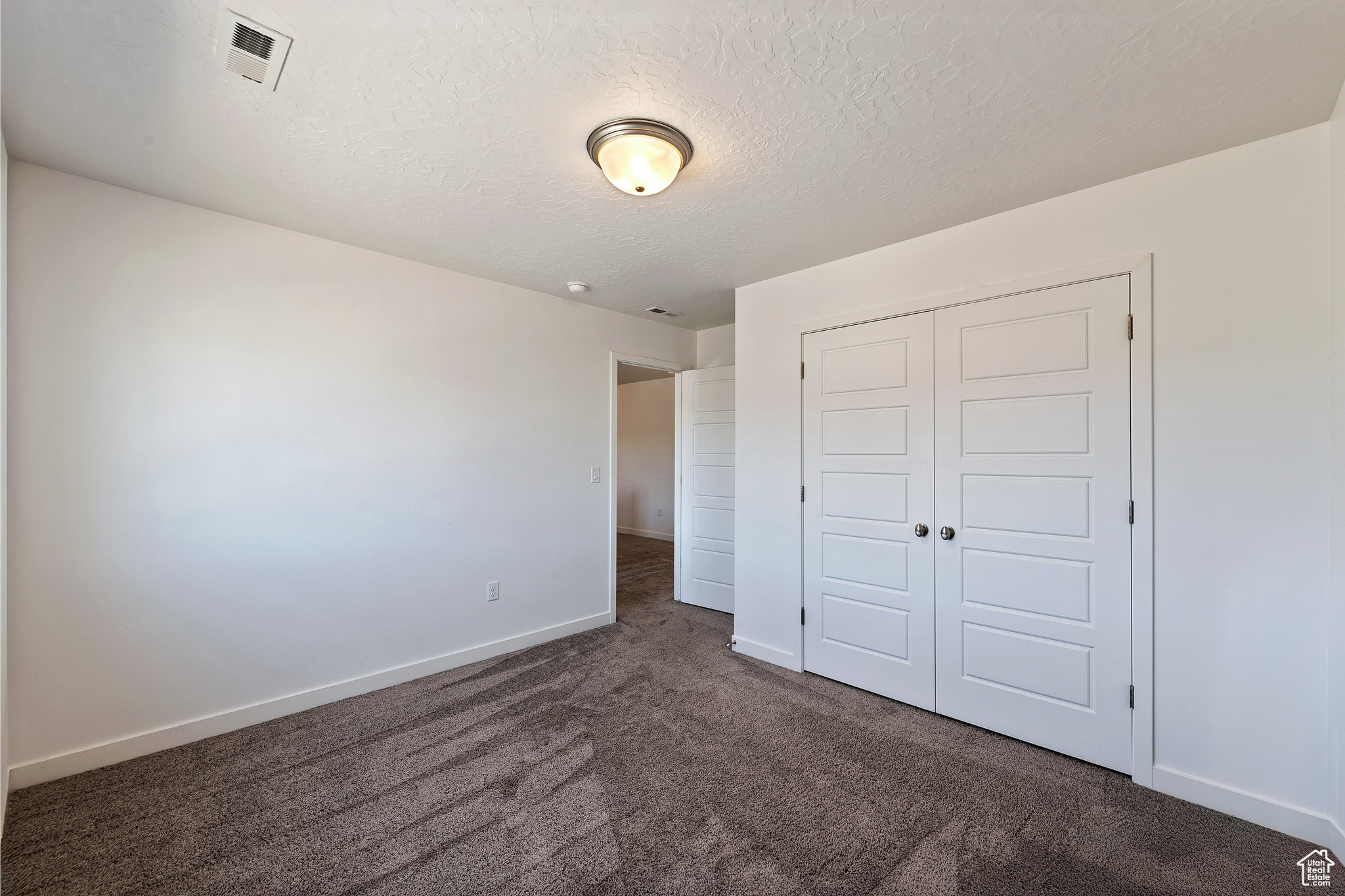 Unfurnished bedroom featuring baseboards, visible vents, carpet floors, a closet, and a textured ceiling