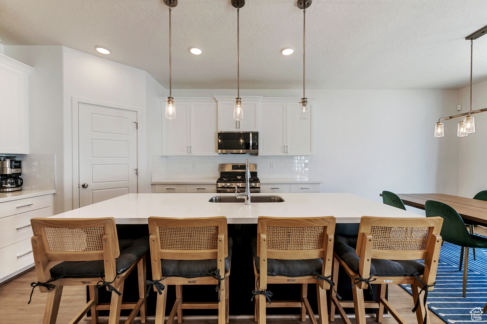 Kitchen featuring a sink, decorative light fixtures, stainless steel appliances, white cabinets, and decorative backsplash